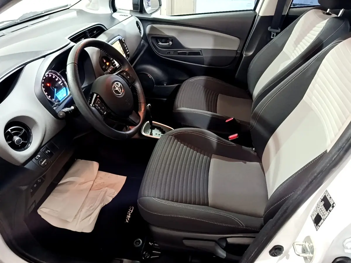 Intérieur avant droit de Toyota Yaris blanche, volant multifonctions cuir, sièges bi-ton gris clair et foncé.