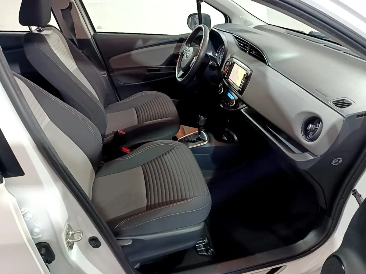 Intérieur avant droit de la Toyota Yaris blanche 2020, sièges bi-ton gris, volant cuir alu et écran tactile navigation.