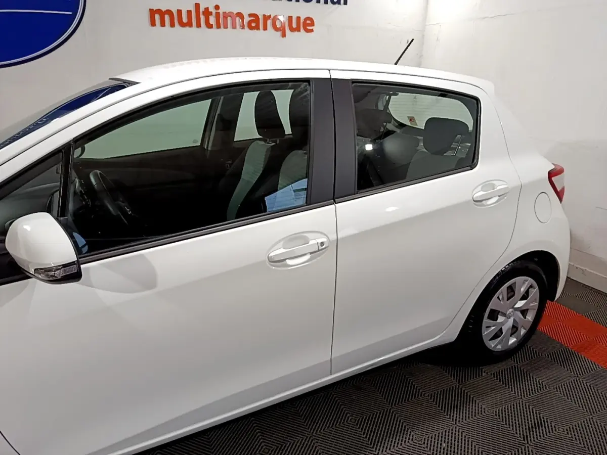 Profil côté gauche d'une Toyota Yaris blanche 2020 hybride, avec rétroviseur blanc et poignées de porte assorties.
