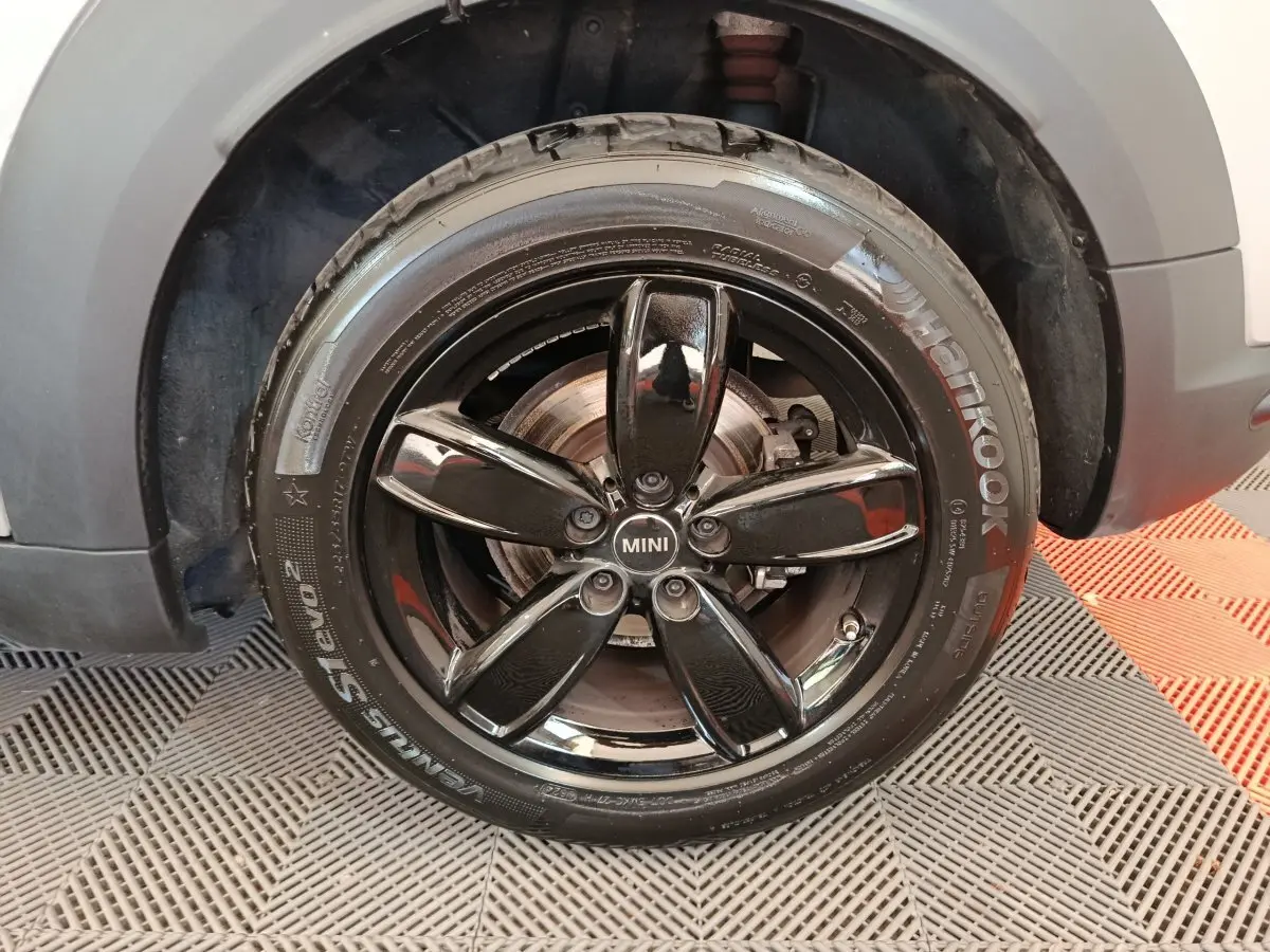 Gros plan sur la roue avant gauche d'une MINI Countryman gris foncé avec jante noire brillante à cinq branches.