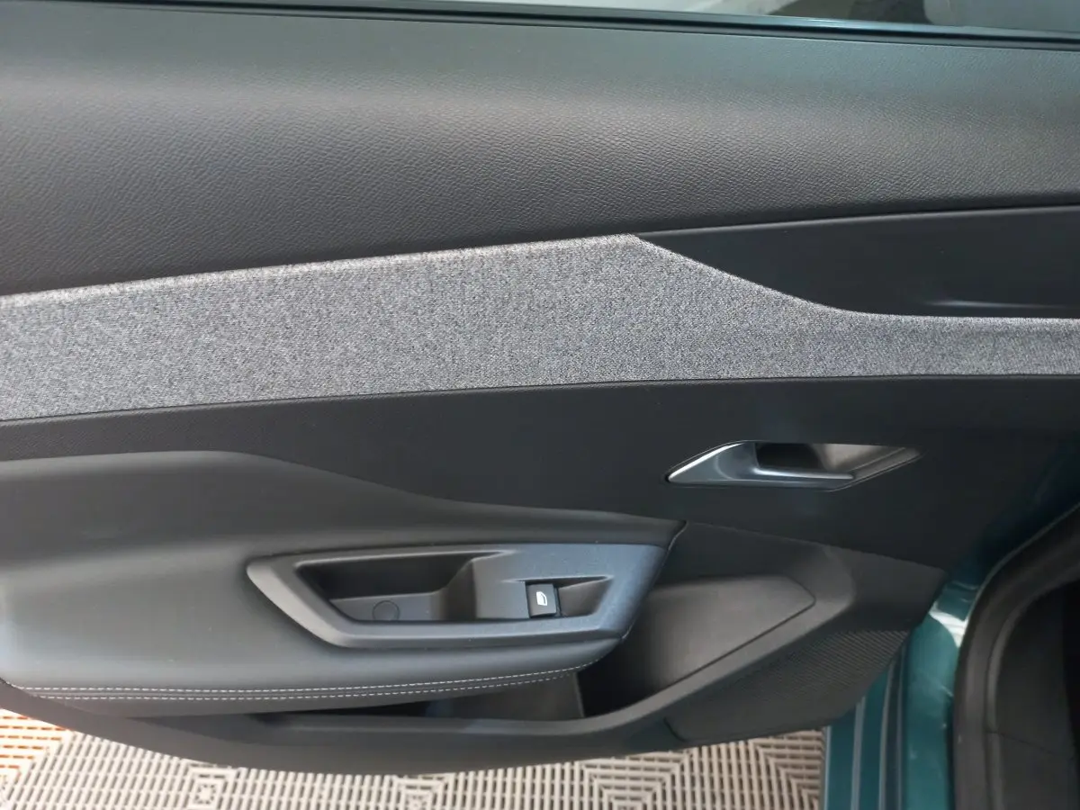 Vue intérieure côté gauche de la porte avant d'une Peugeot 308 bleu, avec poignée argentée et commande de verrouillage.