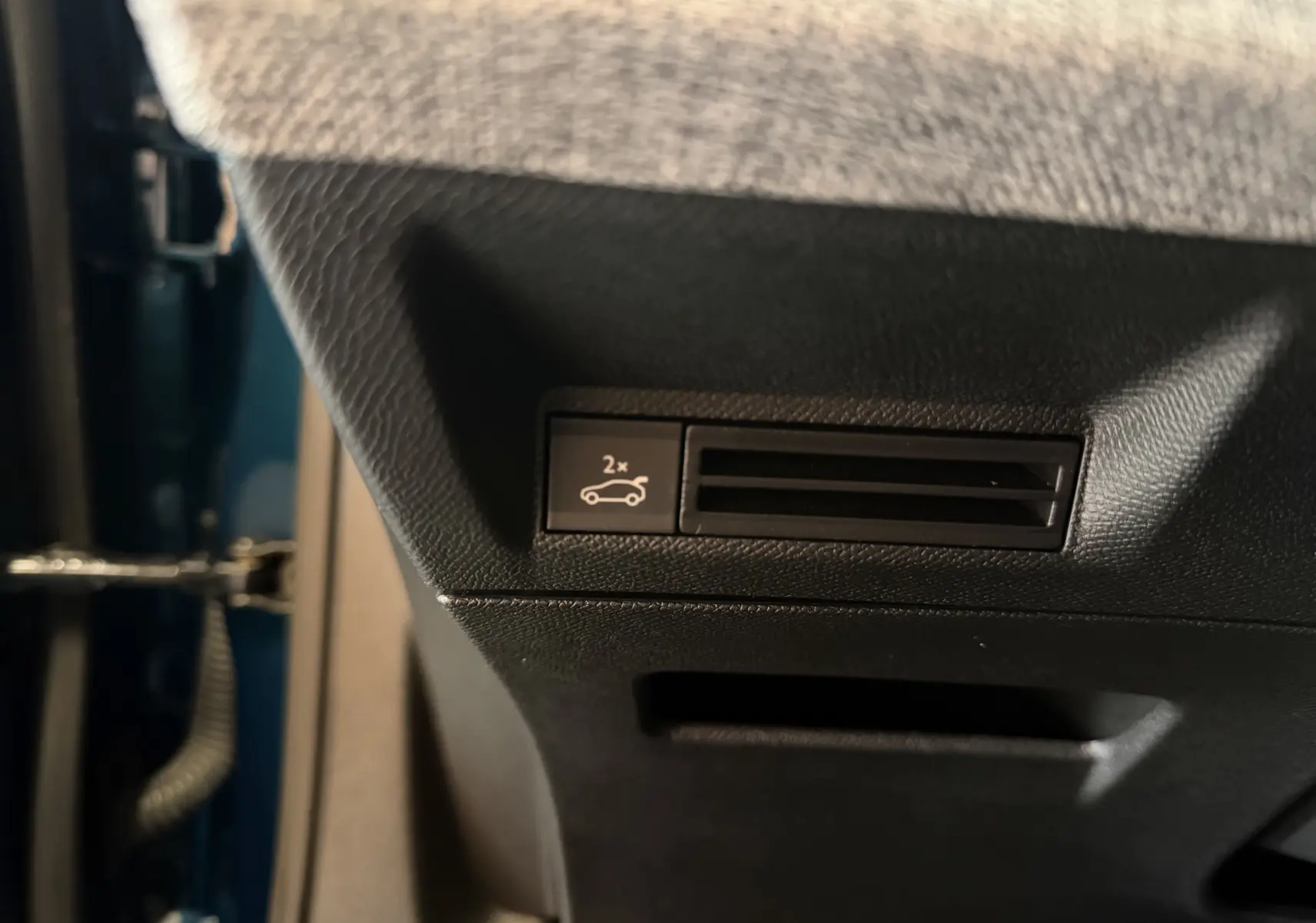 Détail intérieur du bouton d'ouverture du hayon sur la partie inférieure côté conducteur du Peugeot 3008 Hybrid 145 GT bleu obsession.