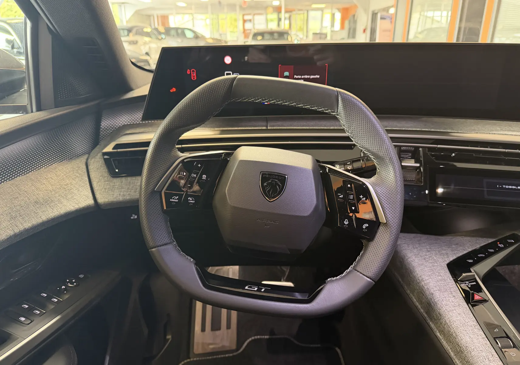 Vue intérieure centrée sur le volant GT du Peugeot 3008 Hybrid 145, avec tableau de bord numérique et sellerie tissu gris.