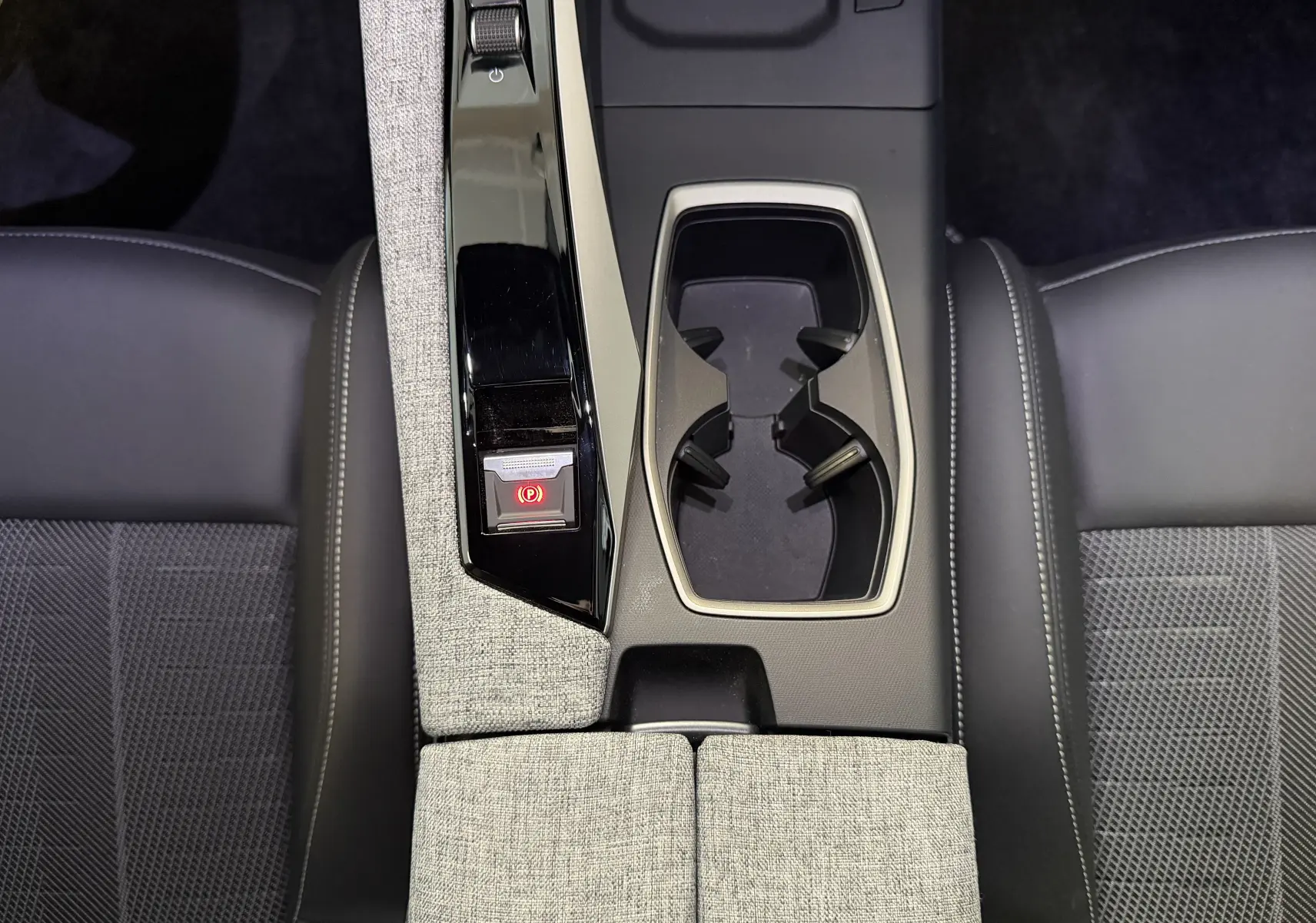 Vue plongeante sur la console centrale du Peugeot 3008 Hybrid 145 GT, avec accoudoirs tissu gris et sièges noirs.