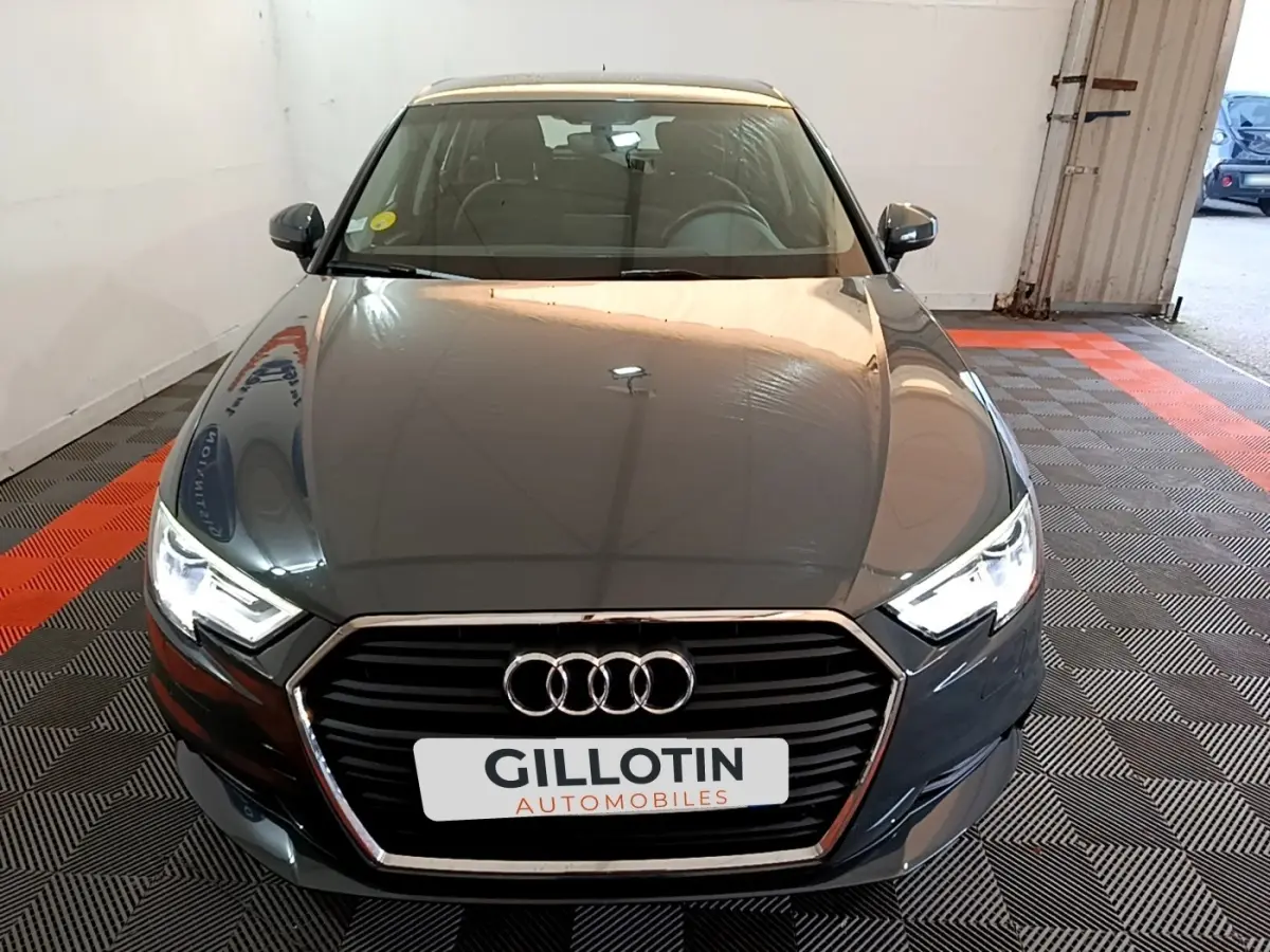 Vue avant d'une Audi A3 30 TDI gris foncé avec phares LED allumés dans un garage.