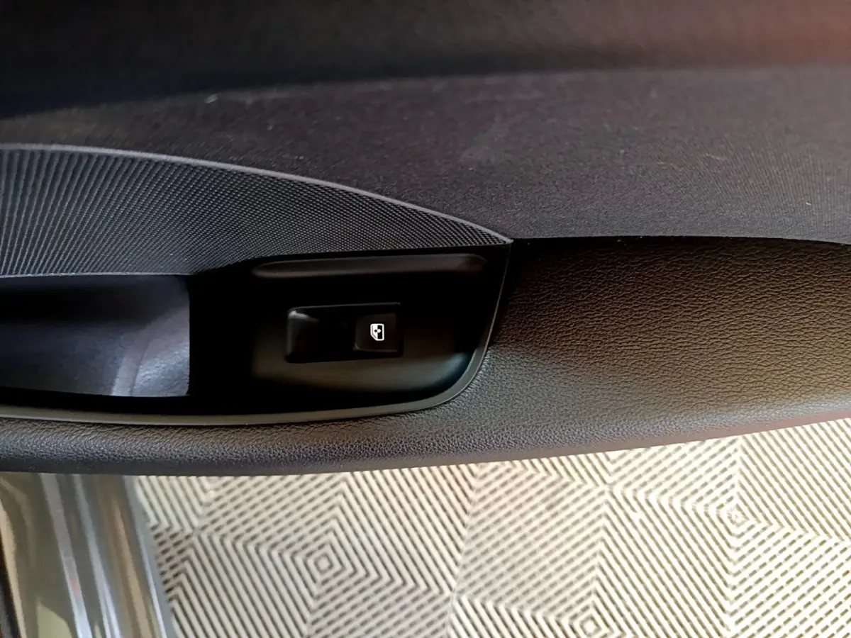 Détail du bouton d'ouverture de coffre sur la porte intérieure côté conducteur d'une Audi A3 gris foncé.