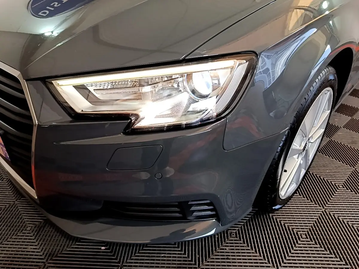 Gros plan sur l'avant droit gris foncé de l'Audi A3 30 TDI 116 S tronic avec phare LED allumé et jante visible.