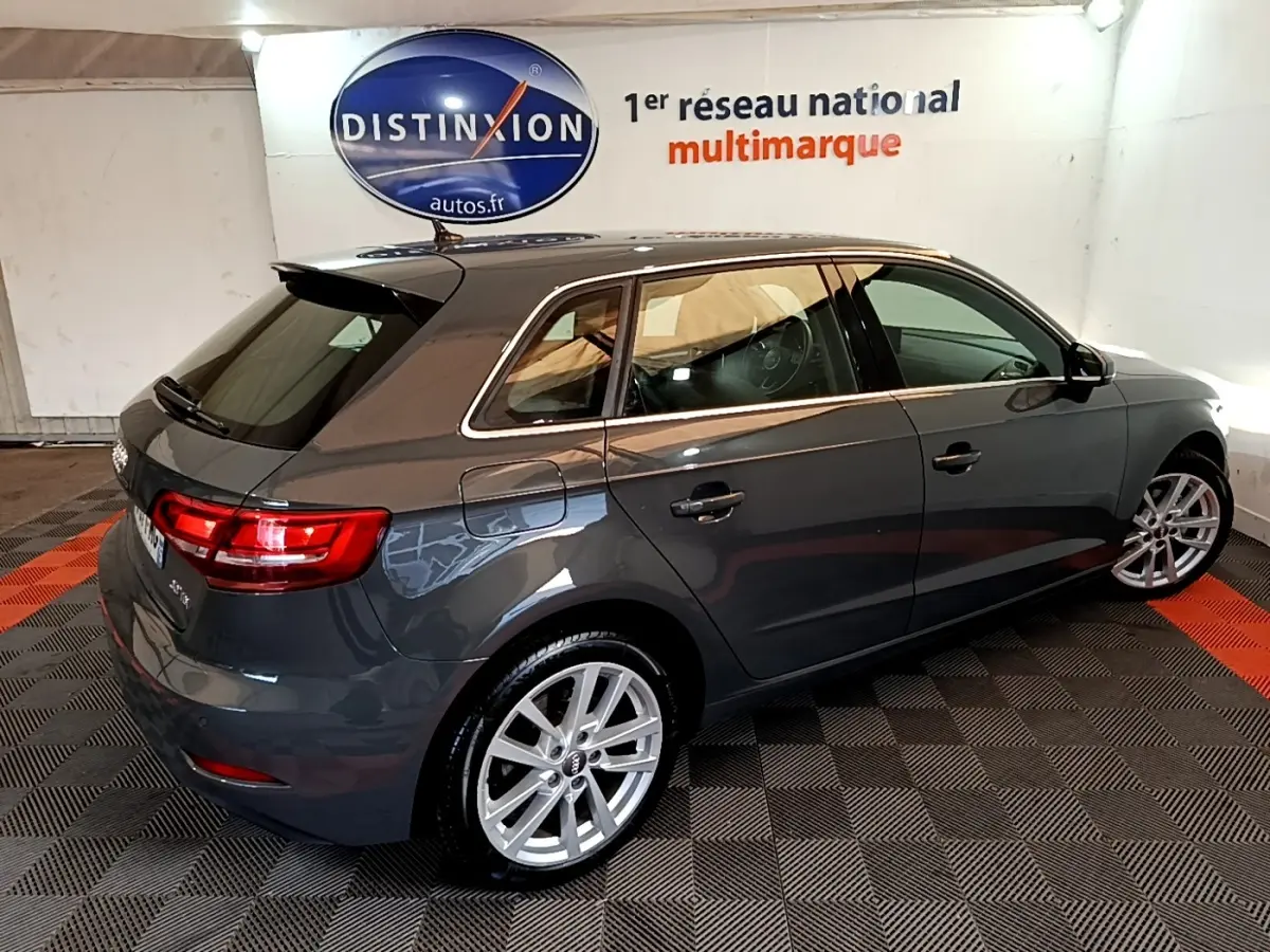 Audi A3 30 TDI gris foncé vue 3/4 arrière droit en intérieur avec jantes alliage et feux arrière allumés.