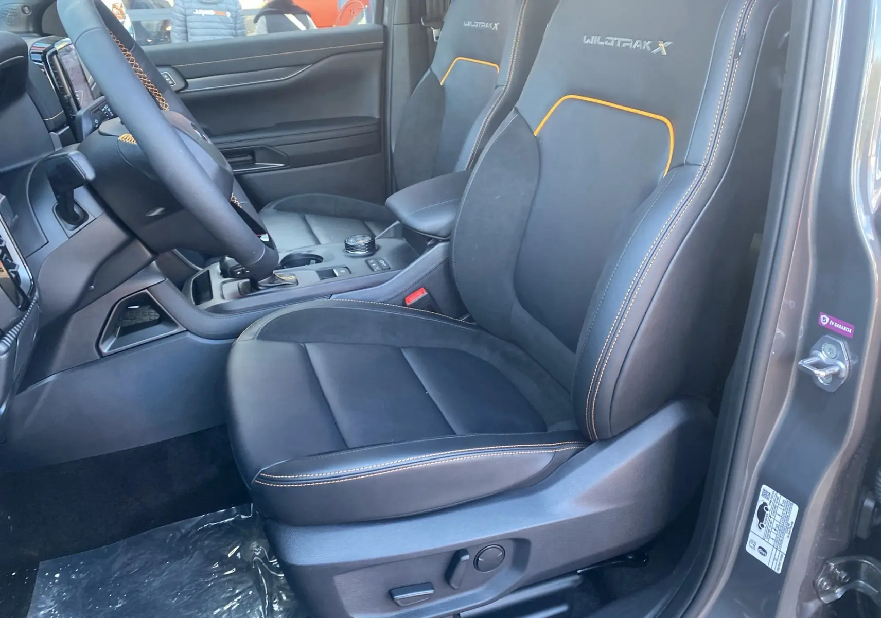 Vue intérieure côté conducteur du Ford Ranger gris carbone, sièges Wildtrak X en cuir noir avec surpiqûres orange.