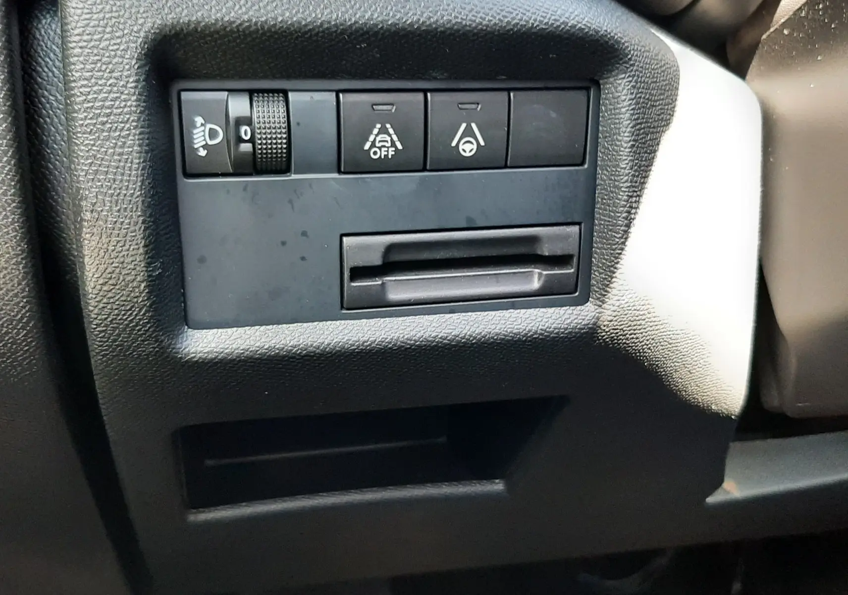 Gros plan sur les commandes de réglage des phares et aides à la conduite, côté gauche du tableau de bord noir du Citroën C5 Aircross gris platinium.