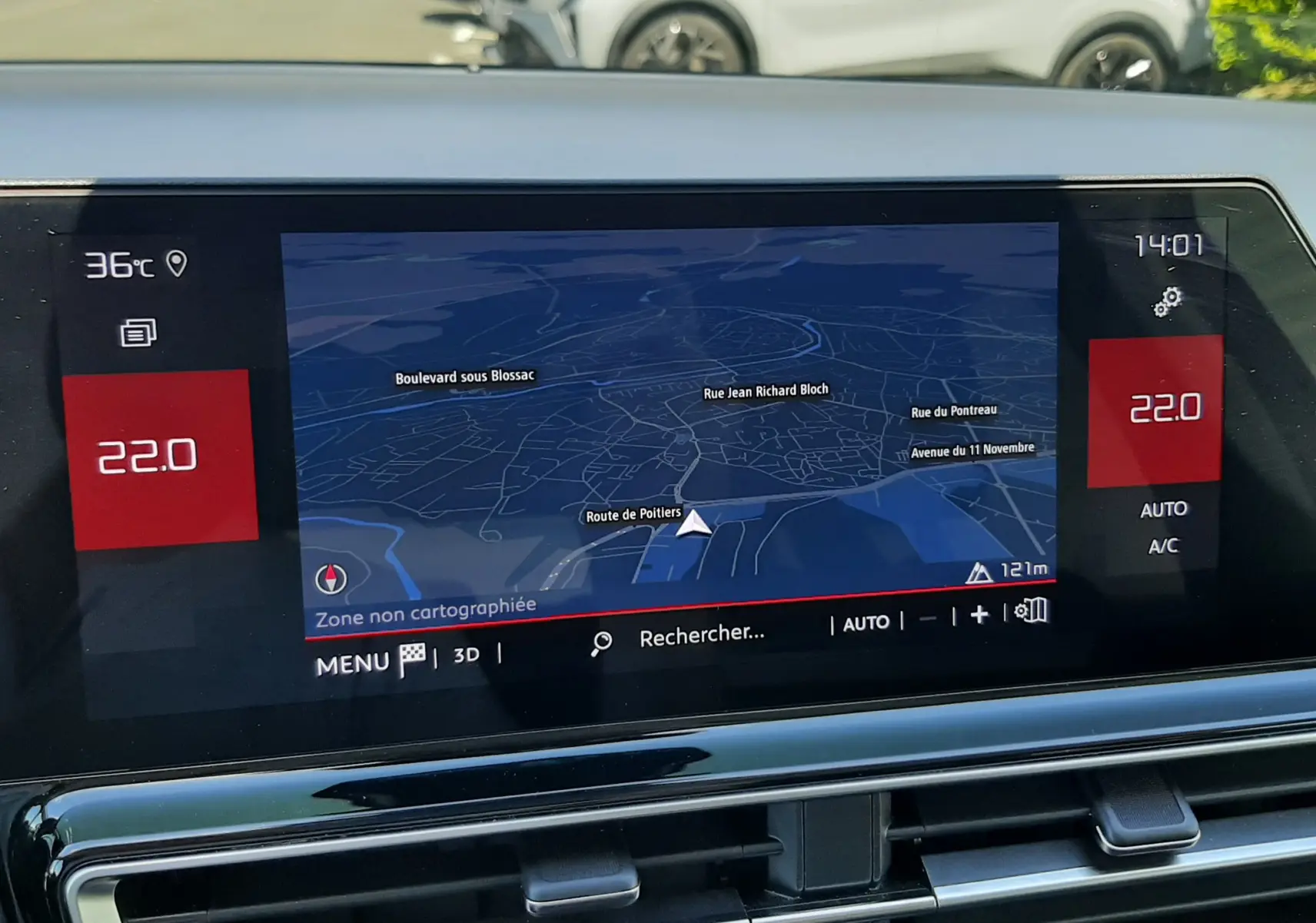 Vue intérieure centrée sur l'écran tactile du tableau de bord avec navigation, en arrière-plan un Citroën C5 Aircross gris platinium stationné.