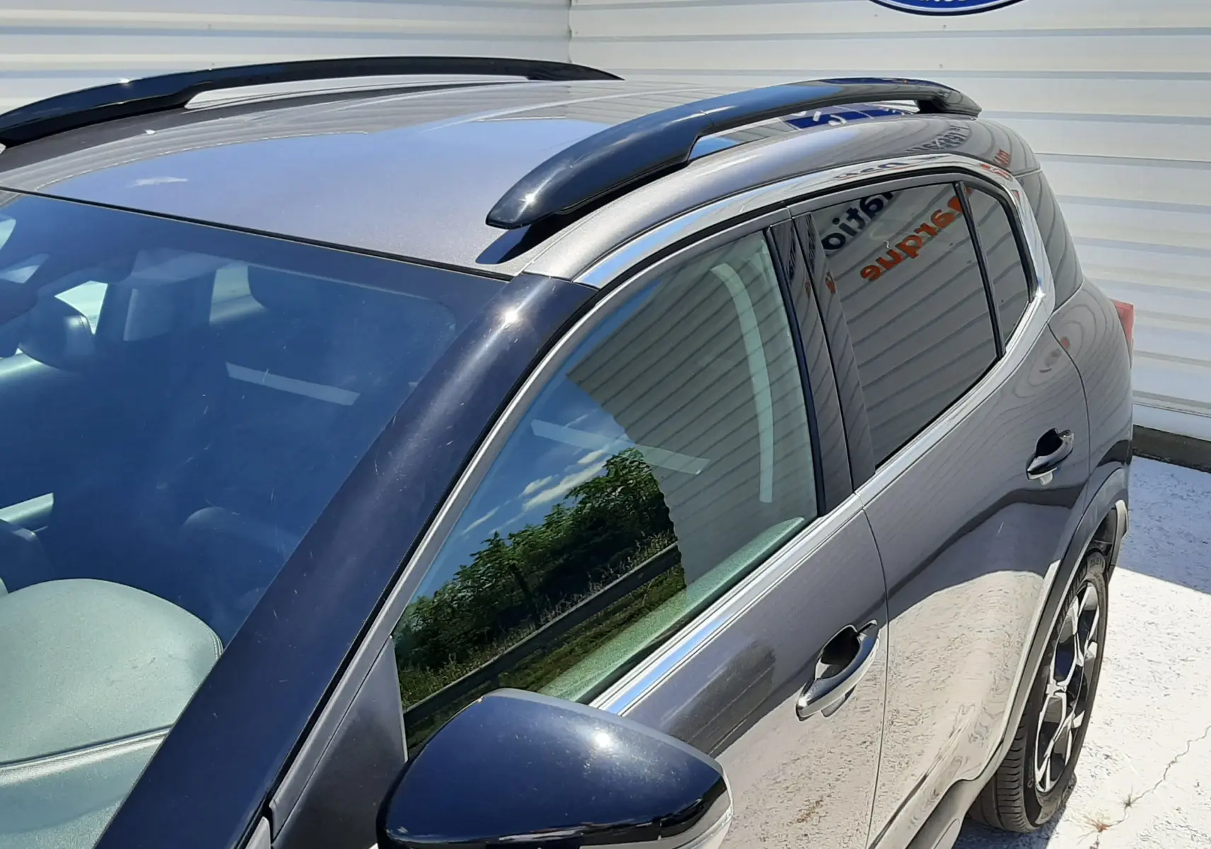 Vue 3/4 avant droit du Citroën C5 Aircross hybride gris platinium avec barres de toit noires et jantes bi-ton.