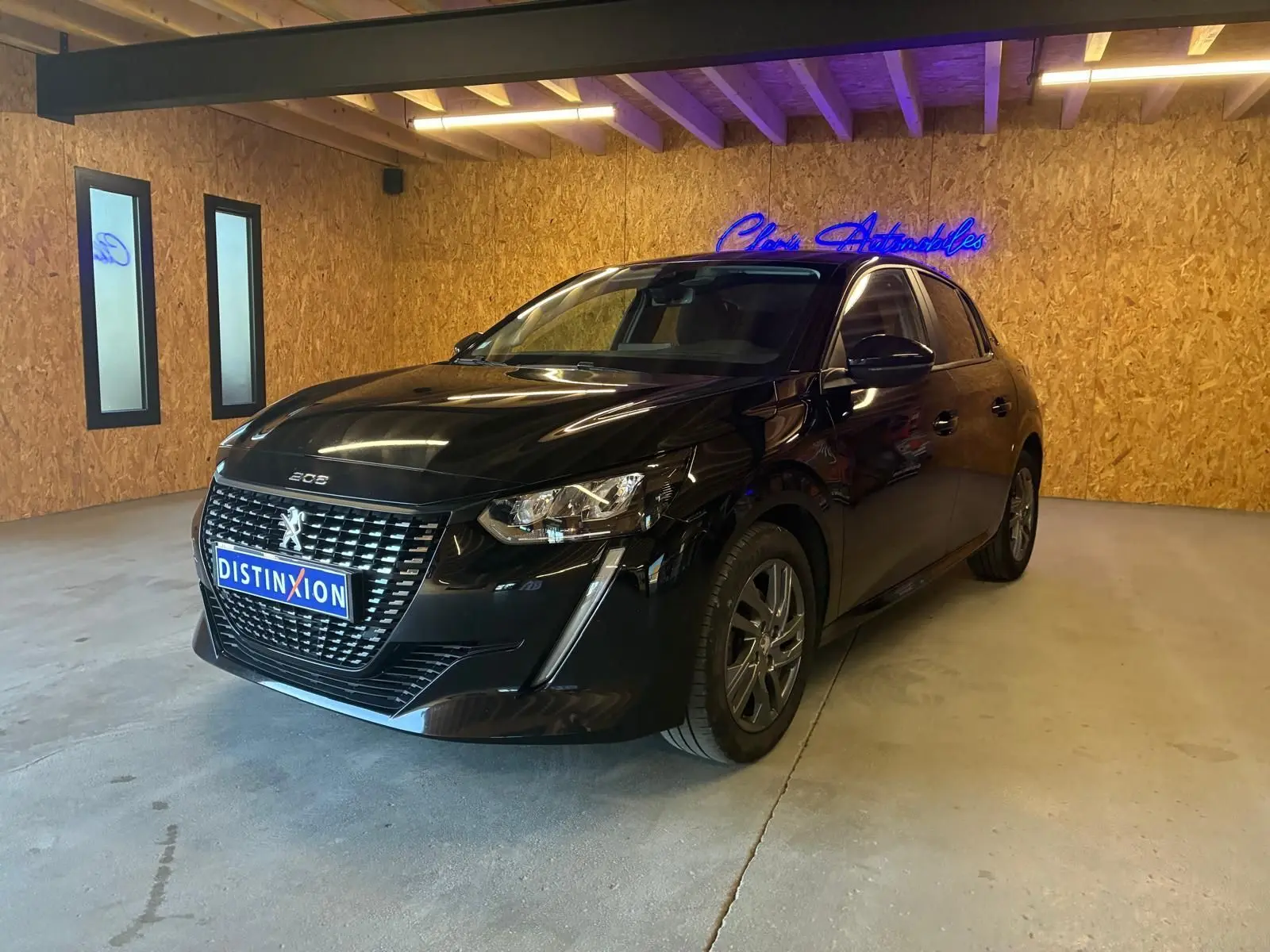 Peugeot 208 1.5 BlueHDi 100 Style noir vue 3/4 avant droit dans un garage avec mur en bois.