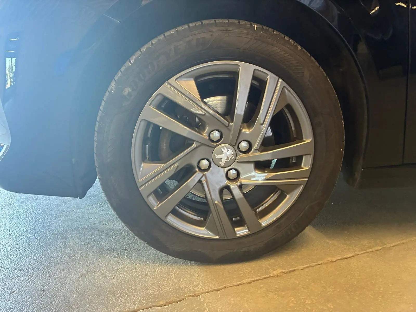 Gros plan sur la roue avant gauche noire d'une Peugeot 208 1.5 BlueHDi 100 Style avec jante alliage grise.