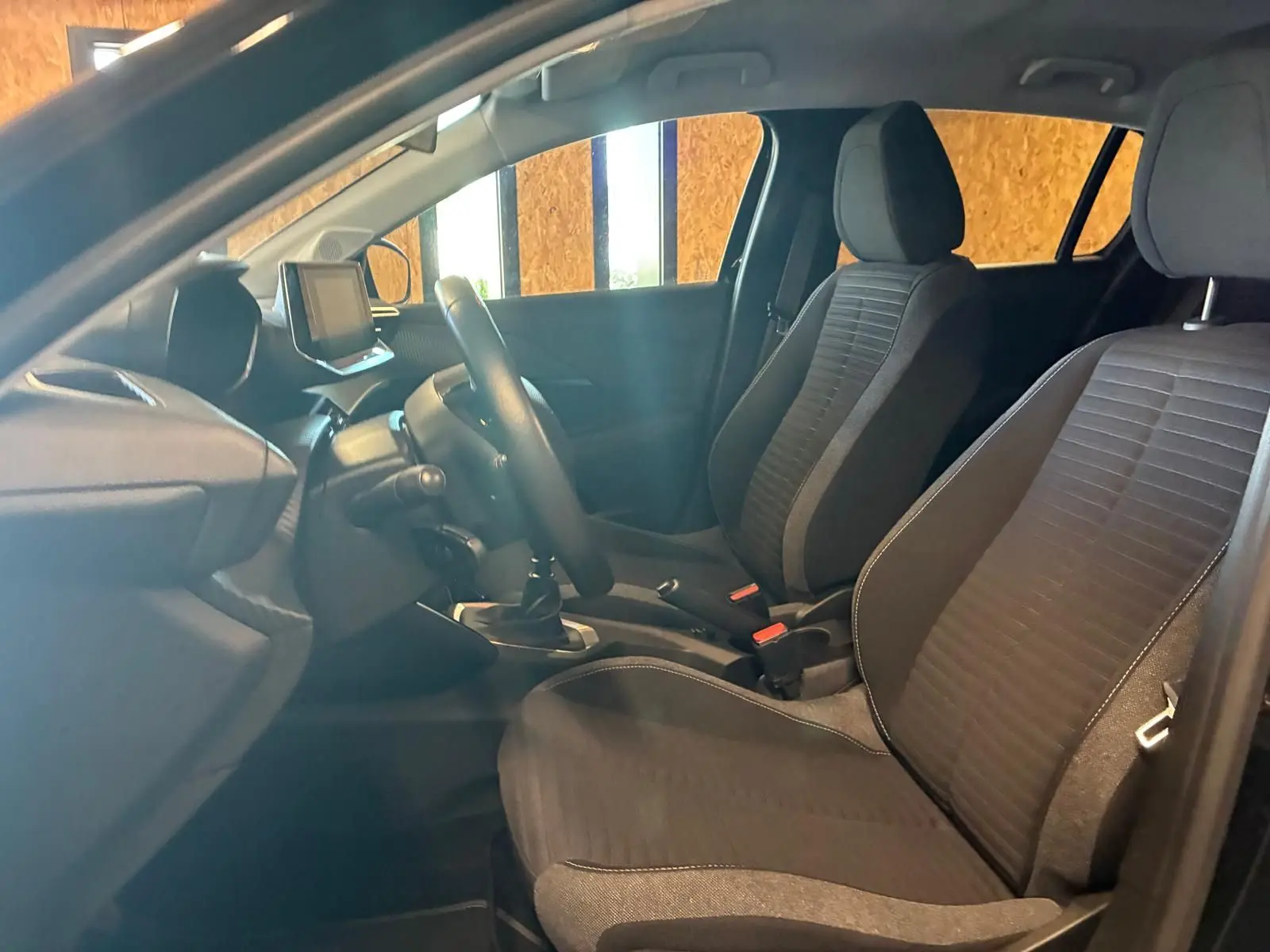Vue intérieure côté conducteur de la Peugeot 208 1.5 BlueHDi 100 Style 2021 avec sièges tissu noirs et tableau de bord moderne.