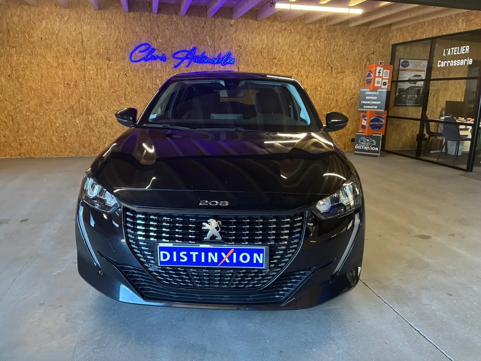 Vue de face d'une Peugeot 208 noire 1.5 BlueHDi 100 Style avec calandre distinctive et plaque Distinxion en intérieur showroom.