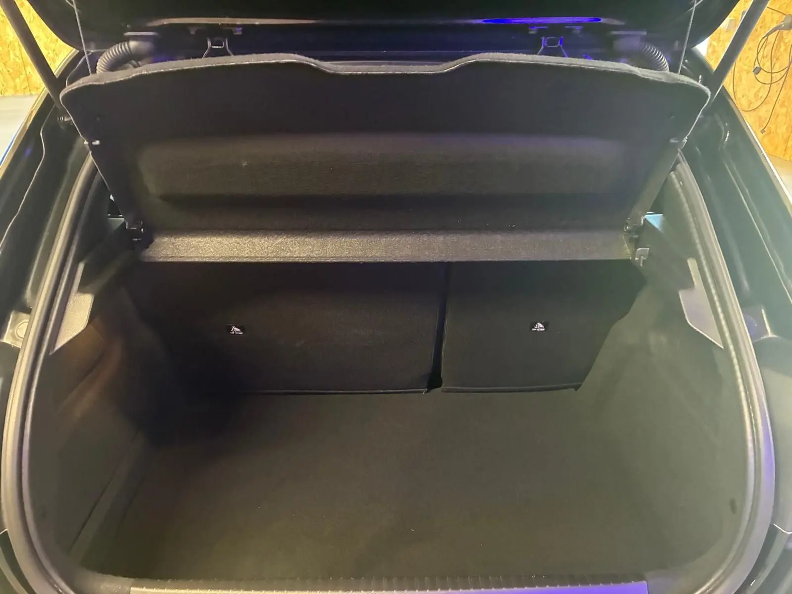 Vue intérieure du coffre ouvert d'une Peugeot 208 noire, montrant un espace de rangement propre et vide.