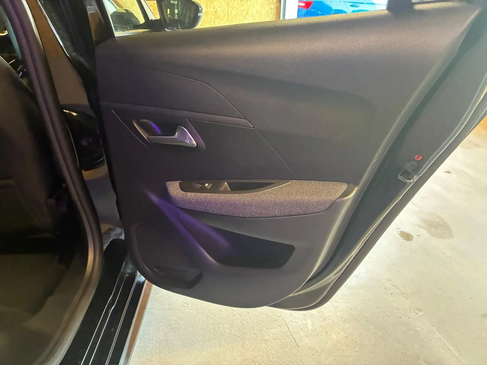 Porte arrière gauche ouverte d’une Peugeot 208 noire 2021, intérieur tissu noir avec poignée argentée.