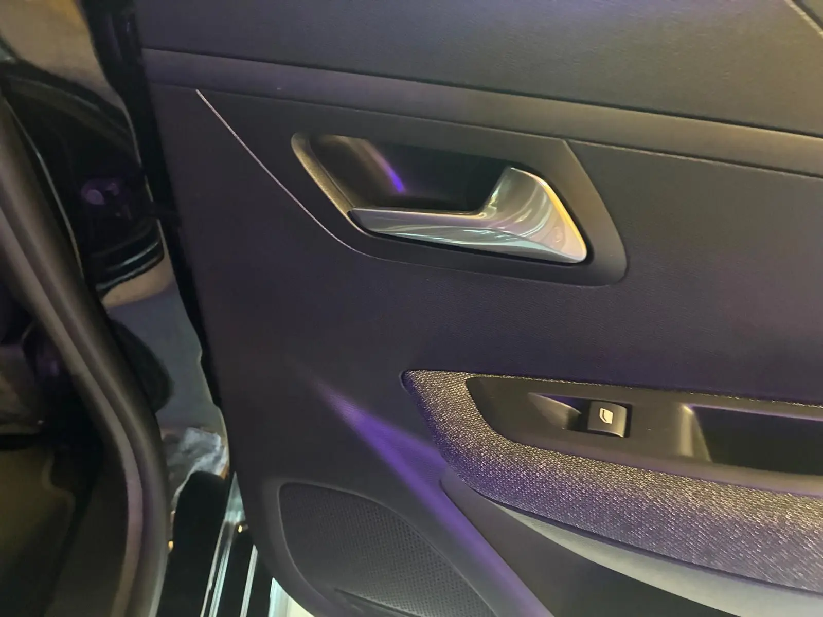 Gros plan sur la porte arrière gauche noire de la Peugeot 208 1.5 BlueHDi 100 Style avec poignée argentée et commande de fenêtre.