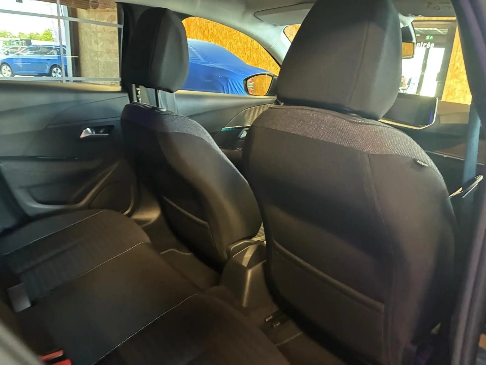 Vue intérieure arrière de la Peugeot 208 noire, montrant les sièges avant en tissu noir et l'habitacle côté droit.