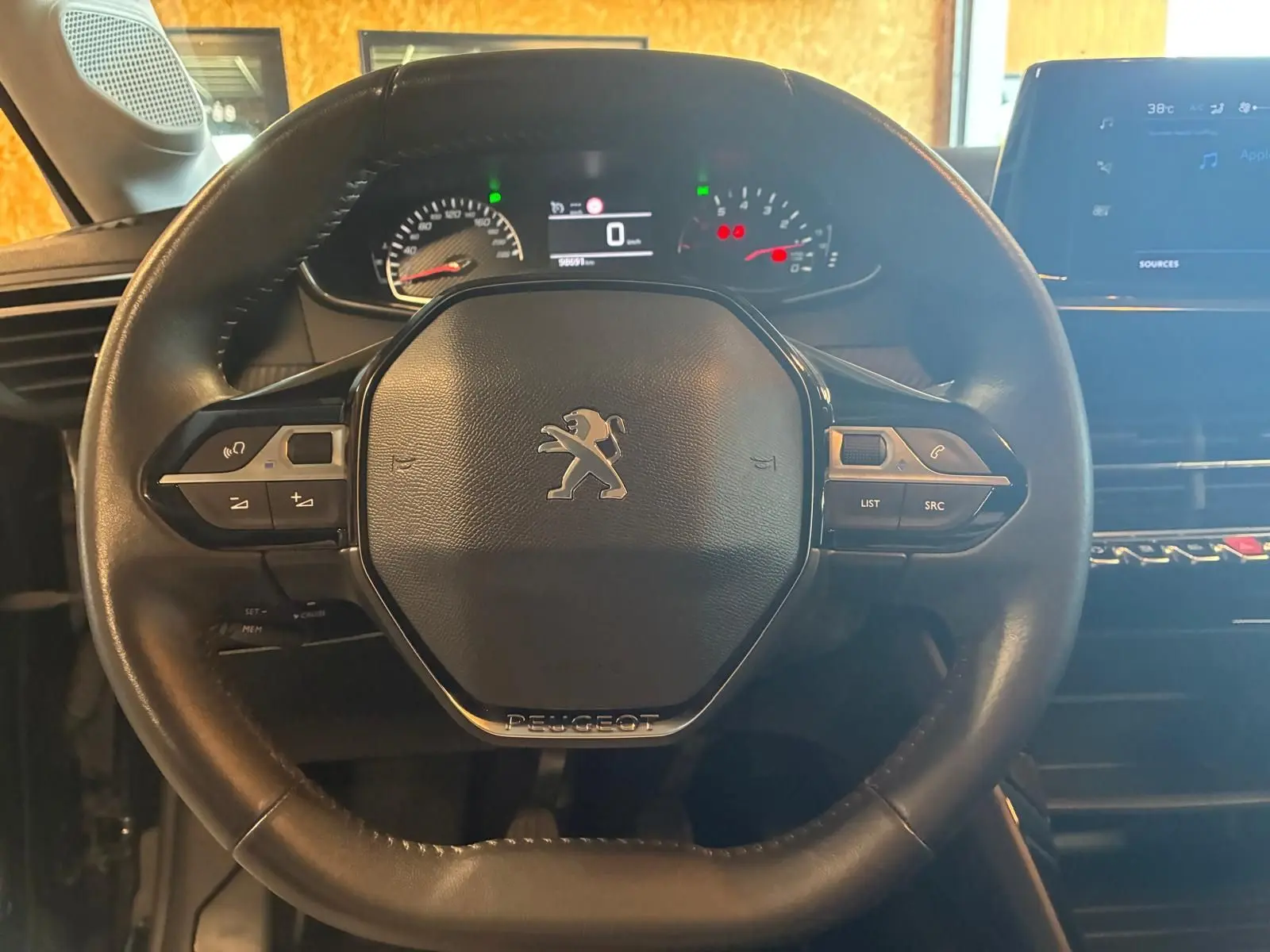 Vue rapprochée du volant noir de la Peugeot 208 1.5 BlueHDi 100 Style avec tableau de bord et écran tactile en arrière-plan.