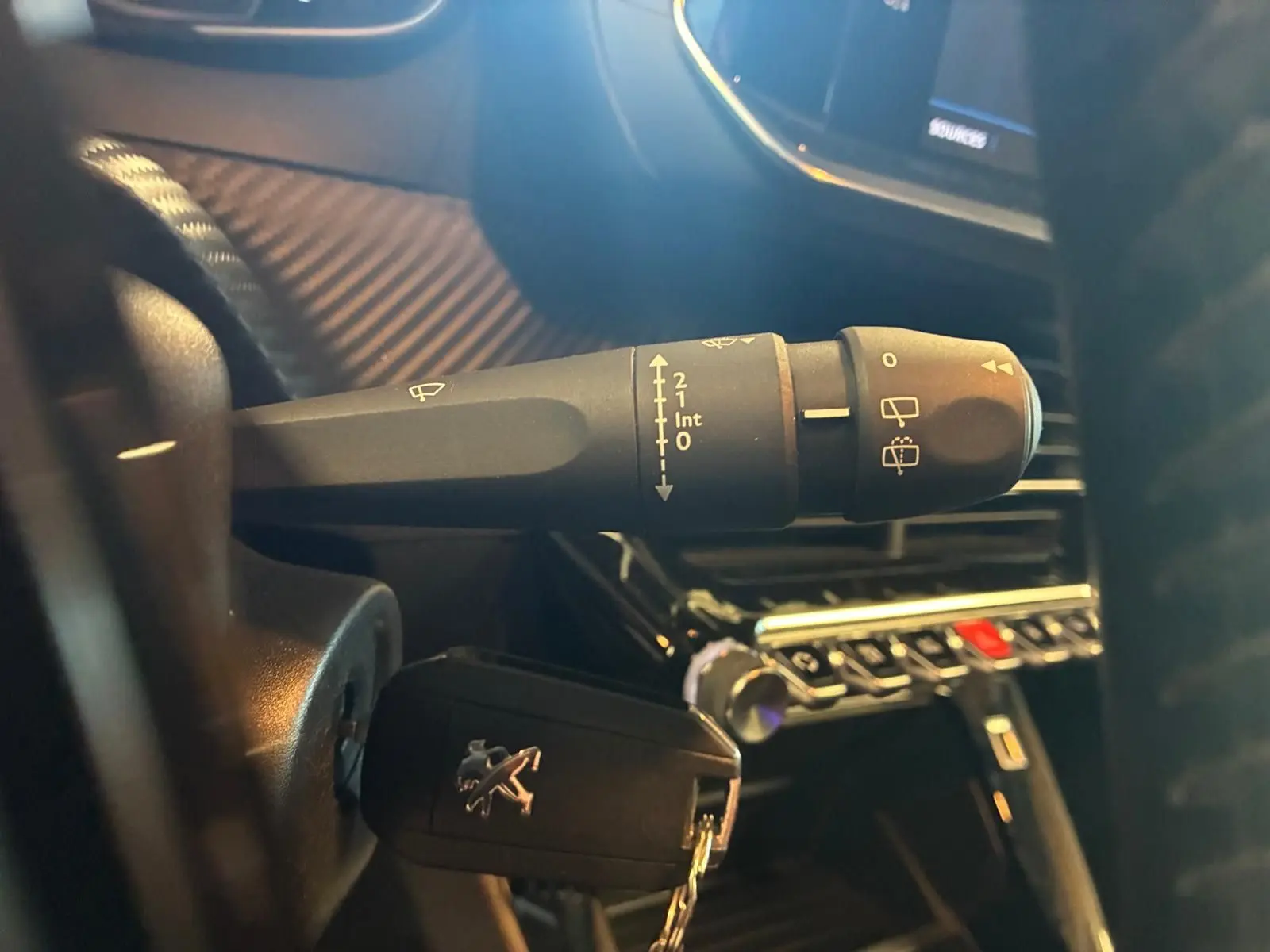 Gros plan sur la manette d’essuie-glace et la clé de contact Peugeot dans l’habitacle noir d’une 208 1.5 BlueHDi.