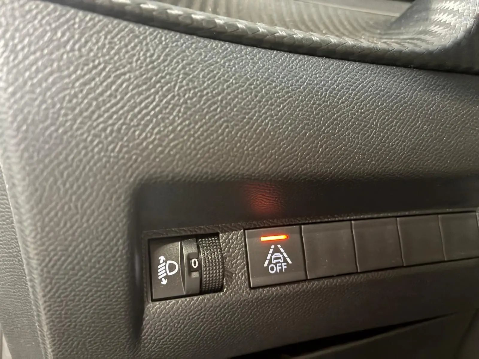 Gros plan sur les commandes noires du tableau de bord d’une Peugeot 208 noire, avec témoin d’alerte allumé.