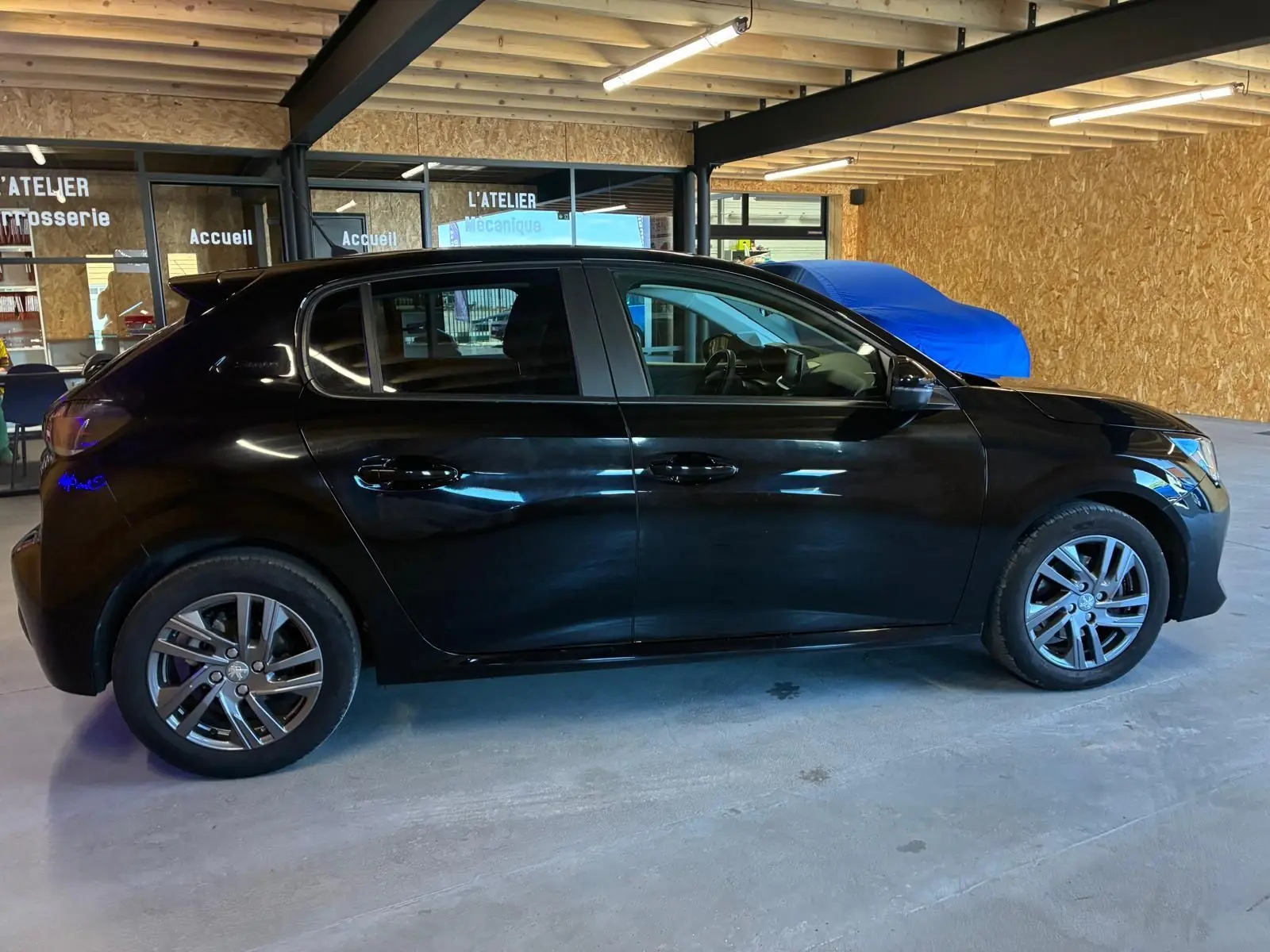 Peugeot 208 1.5 BlueHDi 100 Style noir vue de profil côté gauche dans un garage avec intérieur tissu noir.