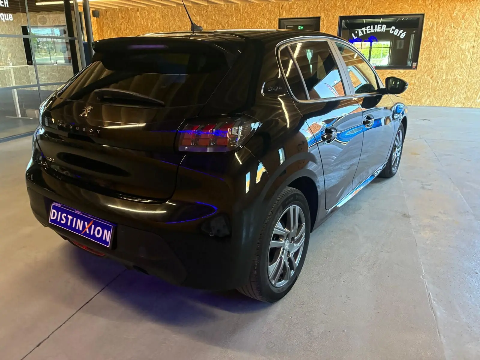 Vue 3/4 arrière droite d'une Peugeot 208 noire 5 portes, avec feux arrière distinctifs et jantes alliage en intérieur clair.