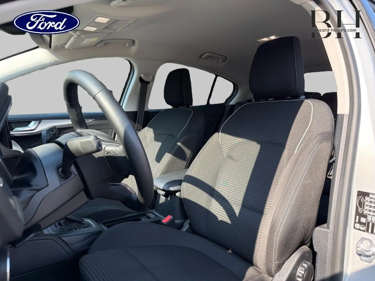 Intérieur avant de la Ford Focus 2023 gris Lunaire, vue côté conducteur avec sièges tissu noir et volant cuir.