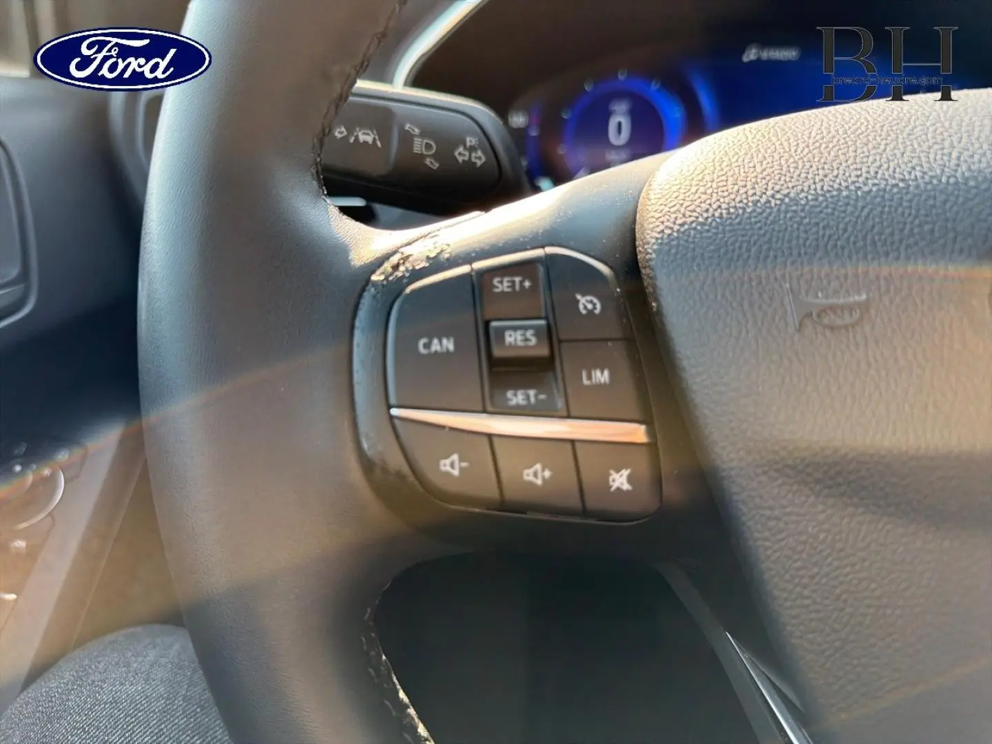Gros plan sur le volant cuir noir de la Ford Focus 2023 avec commandes multifonctions et tableau de bord numérique bleu.