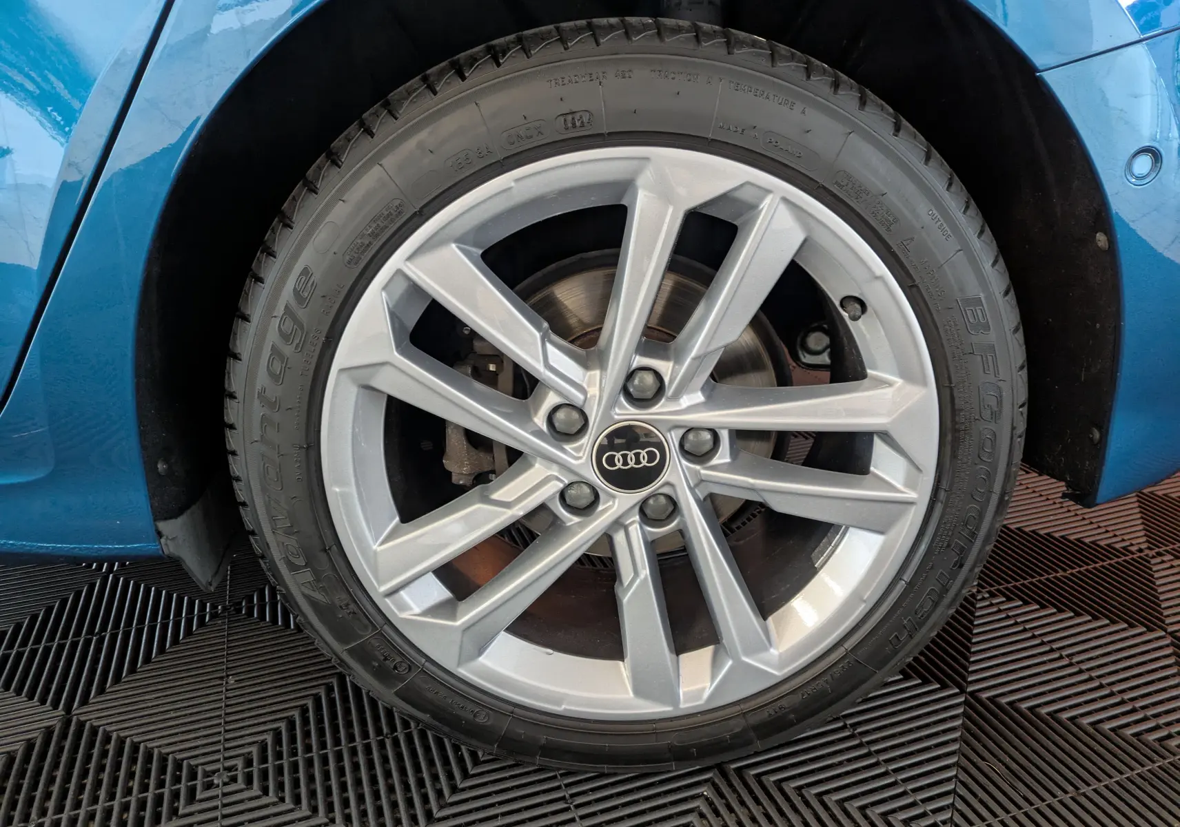 Gros plan sur la roue avant droite de l'Audi A3 Sportback bleu Atollblau avec jante alliage 17 pouces et logo Audi central.