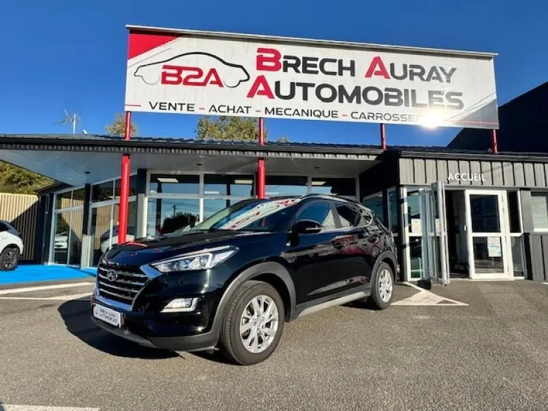 Hyundai Tucson Phantom Black 2019 en 3/4 avant droit devant un garage avec enseigne Brech Auray Automobiles.