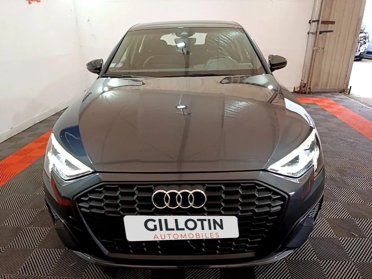 Audi A3 35 TFSI gris foncé vue de face, avec calandre hexagonale noire et phares LED allumés.