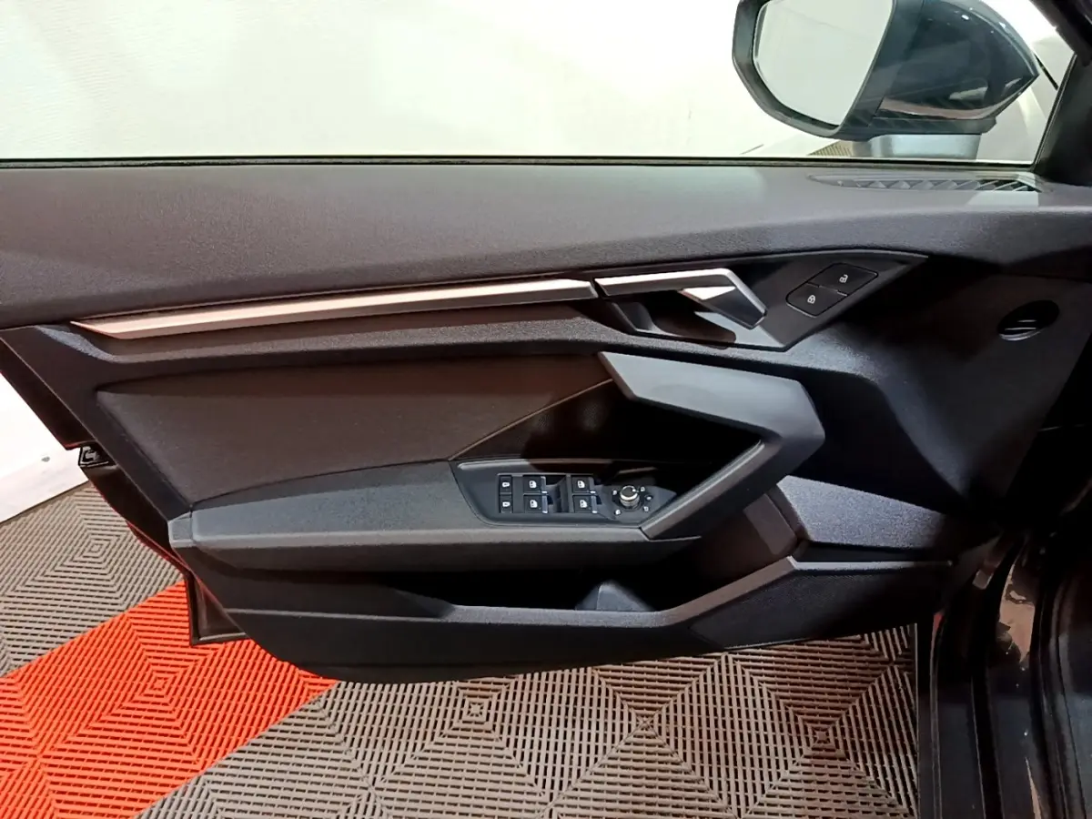 Vue intérieure côté gauche de la porte Audi A3 gris foncé, avec commandes électriques et poignée argentée.