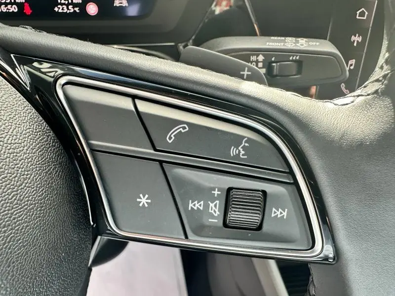 Gros plan sur les commandes multifonctions noires du volant cuir d'une Audi A3 Sportback 30 TFSI 2024.