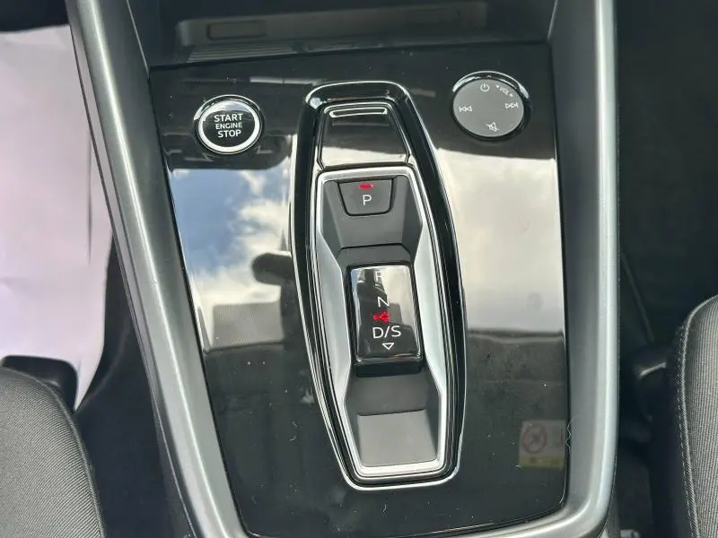 Gros plan sur la console centrale noire brillante de l'Audi A3 Sportback 2024, avec sélecteur de boîte auto et bouton start/stop.