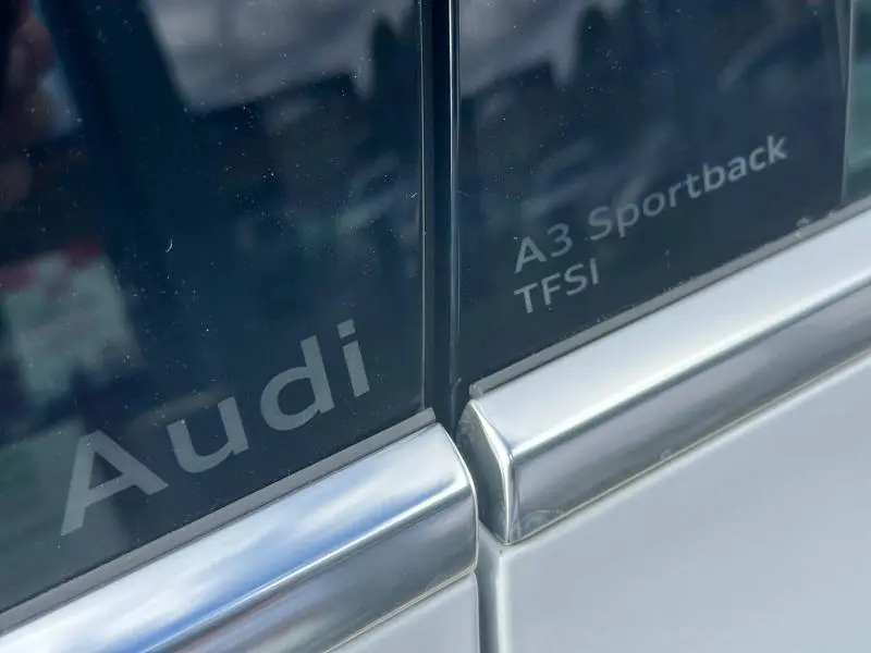 Gros plan sur les vitres arrière argentées d'une Audi A3 Sportback TFSI avec logos gravés sur fond sombre.