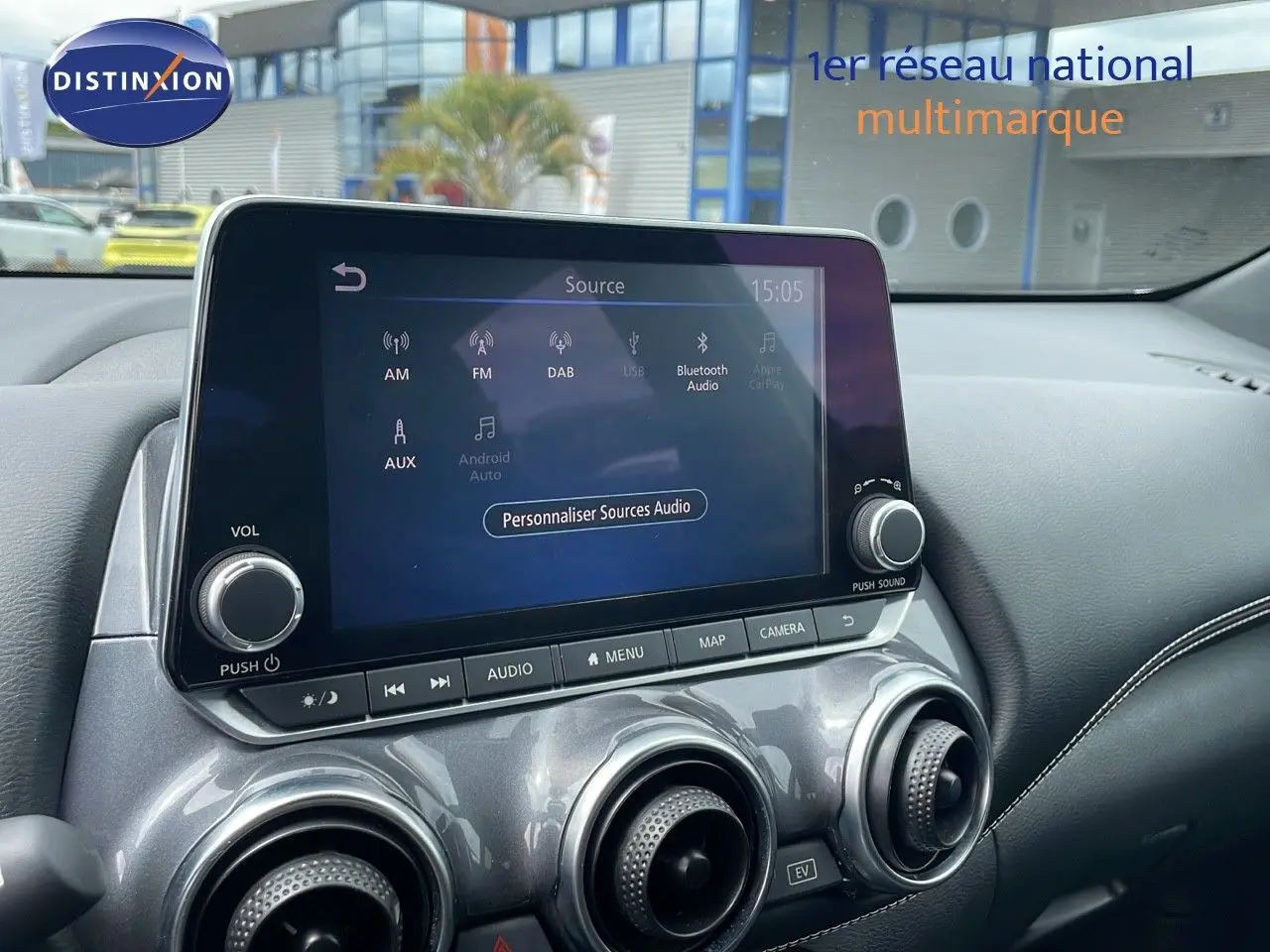 Vue intérieure centrée sur l'écran tactile et les aérateurs ronds du tableau de bord gris perle métallisé du Nissan Juke Hybrid 2023.