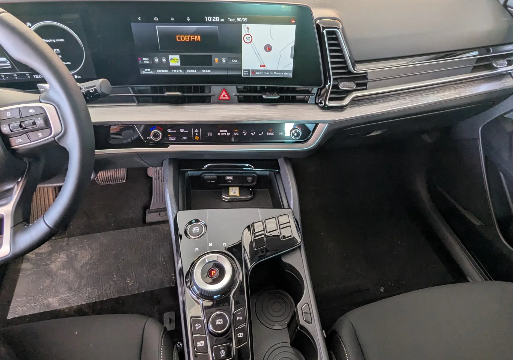 Intérieur du Kia Sportage 2025 vue du poste de conduite, avec écran tactile 12,3’’ et console centrale noire brillante.