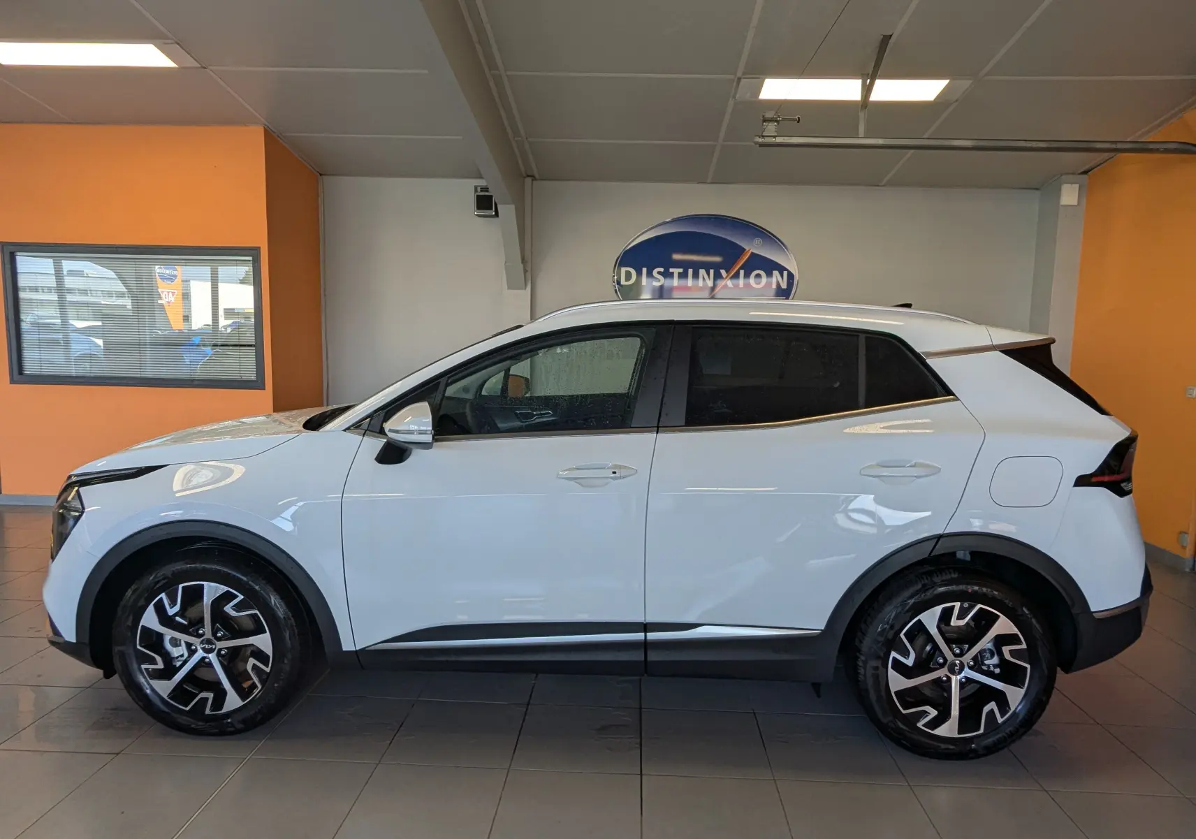 Profil droit du Kia Sportage blanc 2025 en intérieur, avec jantes alliage bicolores et rétroviseurs blancs.