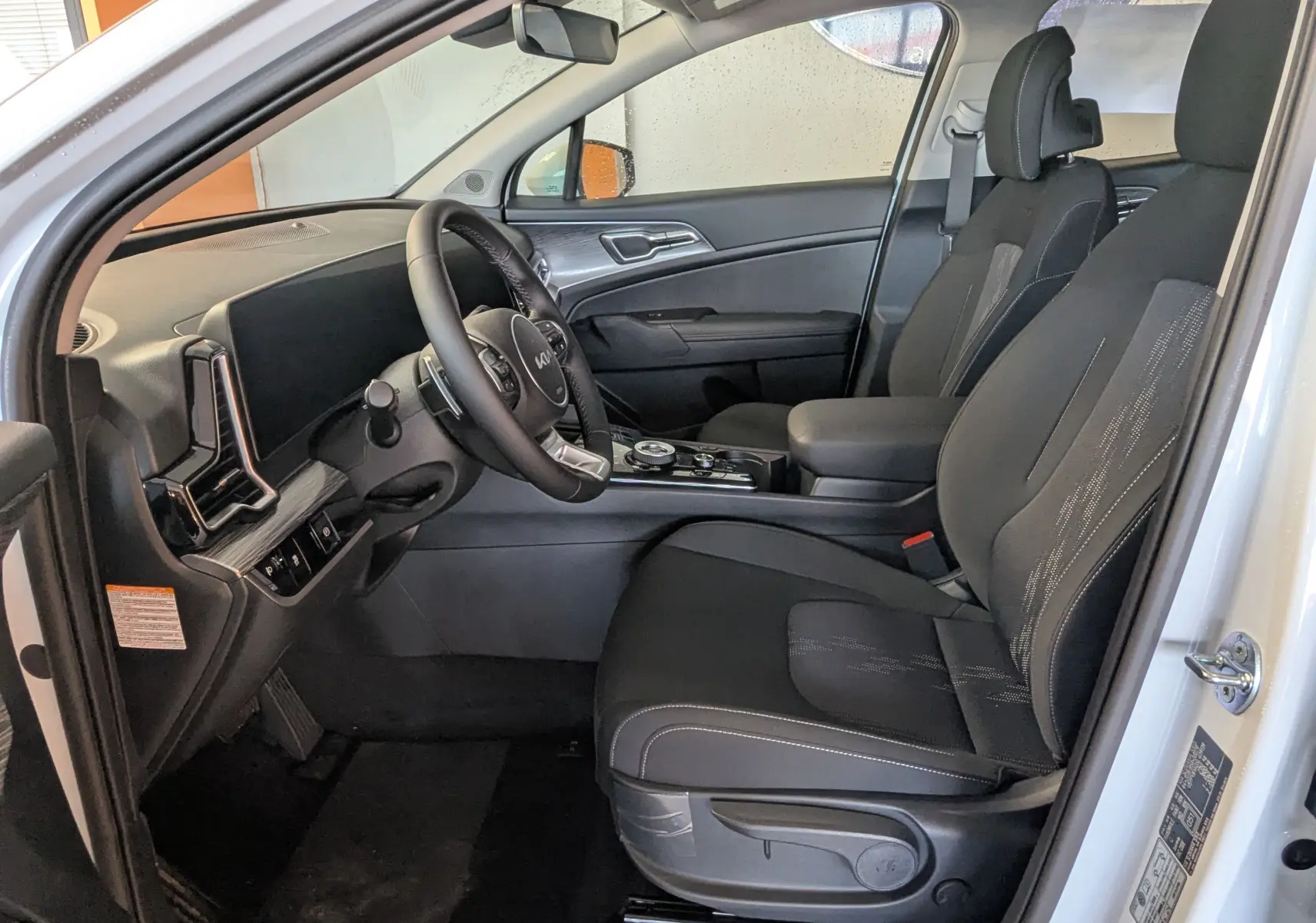 Intérieur côté conducteur du Kia Sportage blanc 2025, sièges noirs avec console centrale et volant multifonctions.