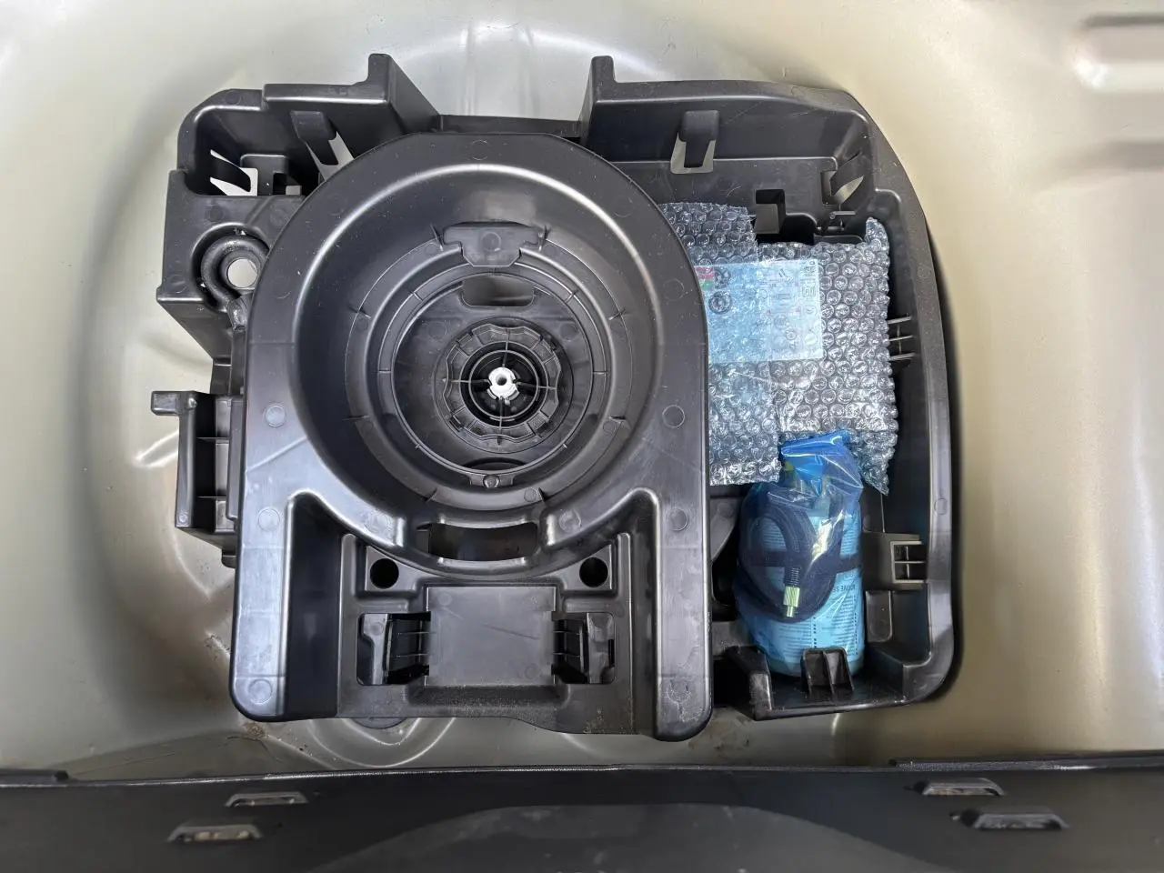 Vue de dessus du compartiment de rangement sous le coffre d'une Citroën C3 gris avec kit de réparation pneus et outils.