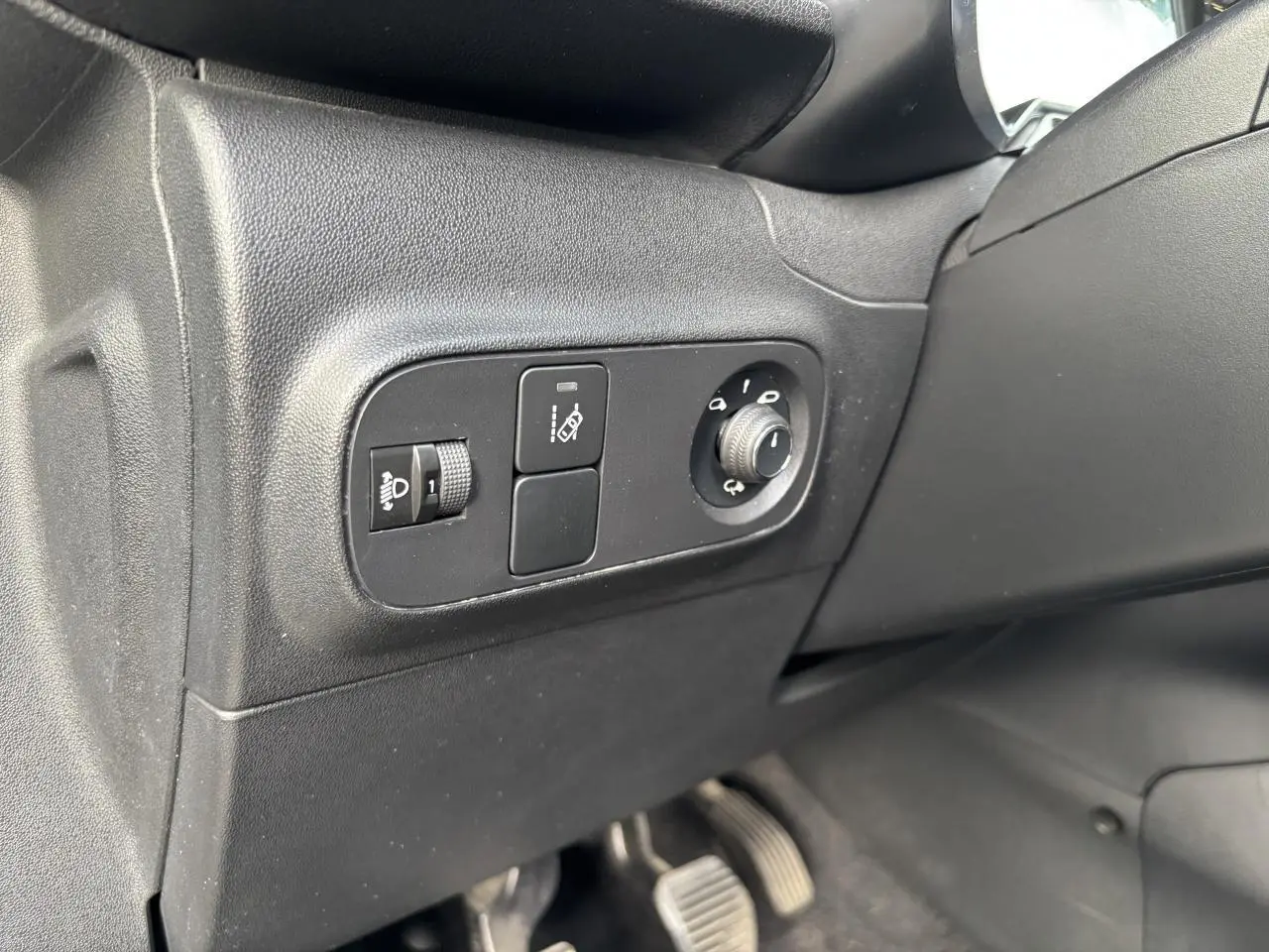 Gros plan sur les commandes de réglage des phares et des rétroviseurs côté conducteur d'une Citroën C3 gris avec toit rouge.