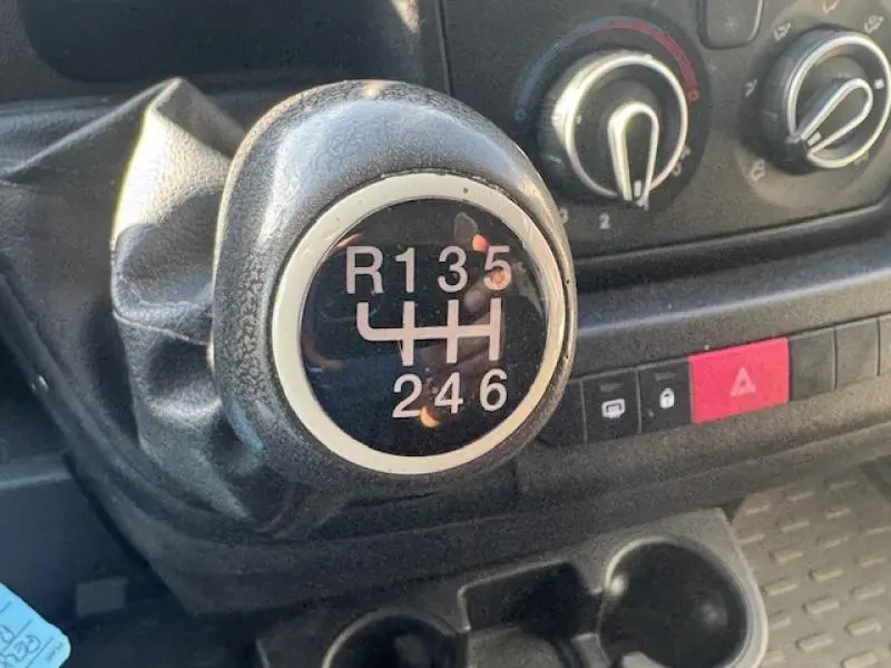 Gros plan sur le levier de vitesses manuel noir du Peugeot Boxer Fourgon blanc, avec commandes de climatisation en arrière-plan.