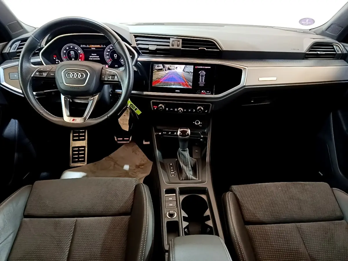 Vue intérieure avant de l'Audi Q3 35 TFSI S Line 2022, tableau de bord moderne avec écran tactile et volant cuir multifonctions.