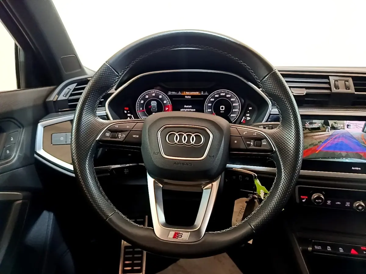 Vue intérieure centrée sur le volant cuir perforé S Line d’un Audi Q3 35 TFSI 150 S Tronic avec tableau de bord digital.