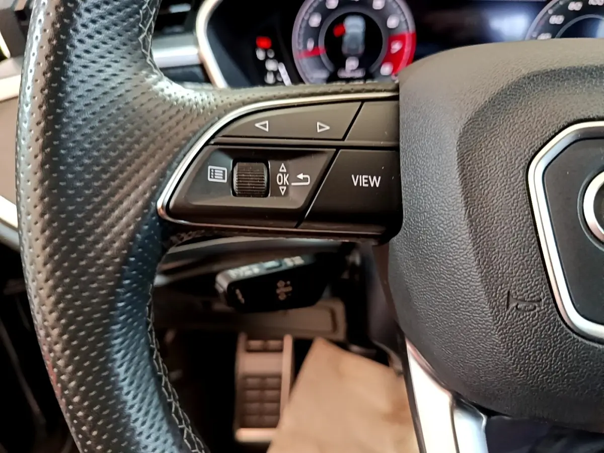 Gros plan sur le volant cuir noir de l'Audi Q3 35 TFSI, avec commandes multifonctions et tableau de bord numérique en arrière-plan.