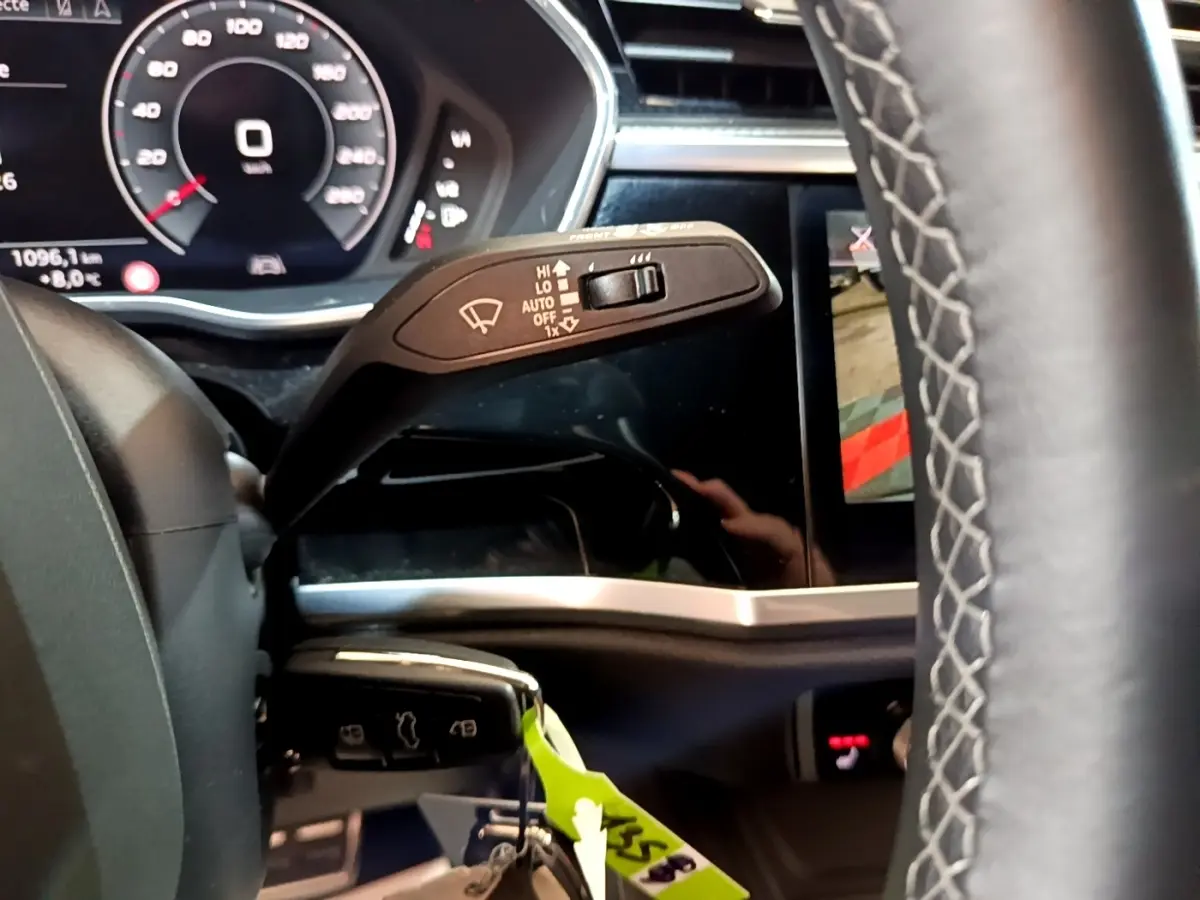 Gros plan sur la manette d’essuie-glace à gauche du volant cuir de l’Audi Q3 gris foncé, tableau de bord digital visible.