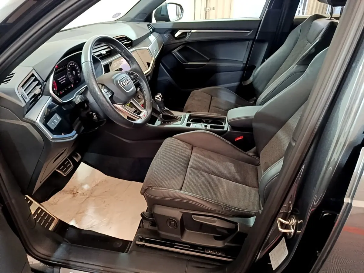 Vue intérieure côté conducteur de l’Audi Q3 gris foncé 35 TFSI S Line, avec volant cuir multifonctions et sièges tissu.
